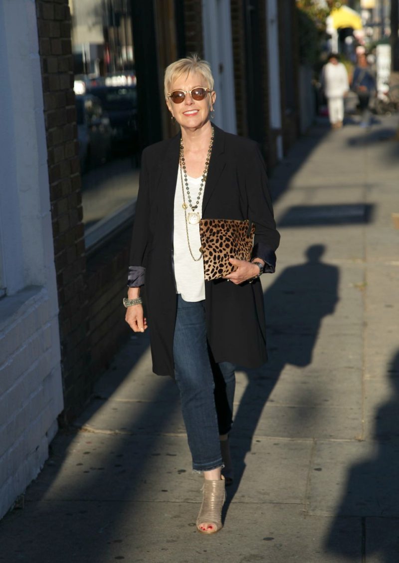 50+ style blogger Susan B. wearing a long navy jacket, layered necklaces and a Clare V leopard bag.