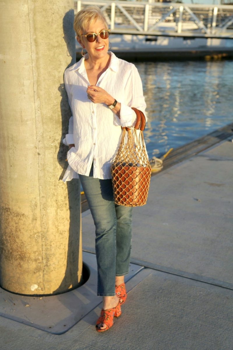 style blogger Susan B. wears an easy white shirt in linen with jeans, a bucket bag and slide sandals. Details at une femme d'un certain âge.