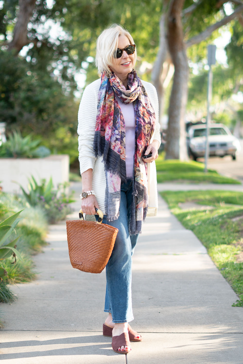 Susan B. of une femme d'un certain age wears an Eileen Fisher cardigan, Tilo floral scarf, lilac sweater, woven leather bag and mauve sandals.