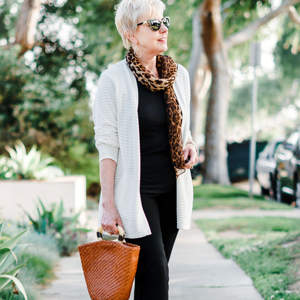 Susan B. of une femme d'un certain age wears a leopard scarf, black tee and pants, a woven leather tote and metallic mules. Details at une femme d'un certain age.