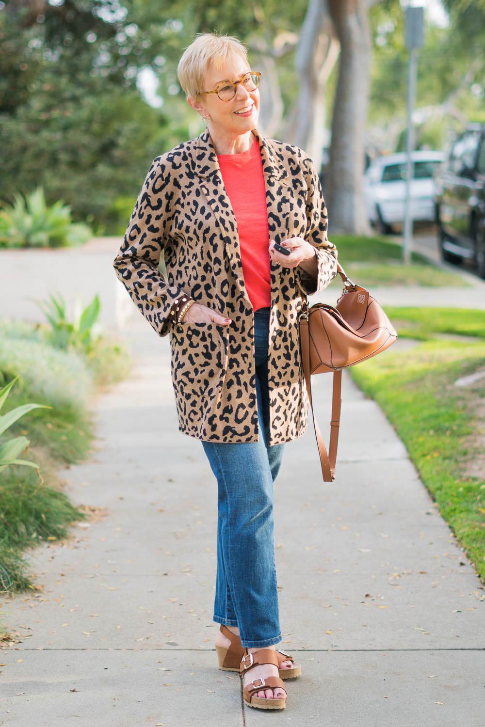 Susan B. of une femme d'un certain age wears a leopard sweater jacket with a coral tee, jeans, and Loewe puzzle bag.