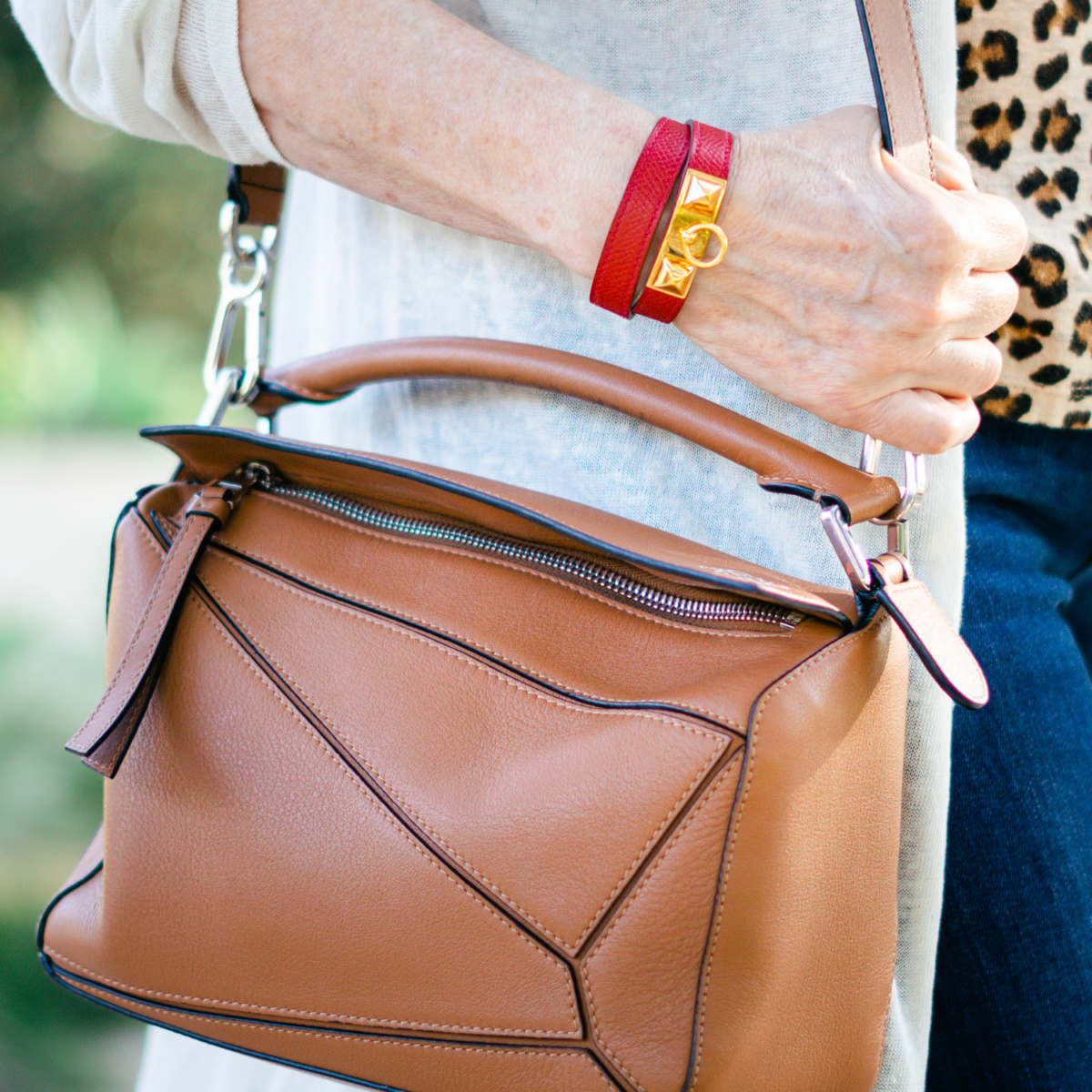 Detail: Susan B wears a red Hermes Rivale bracelet and a Loewe small puzzle bag. Info at une femme d'un certain age.