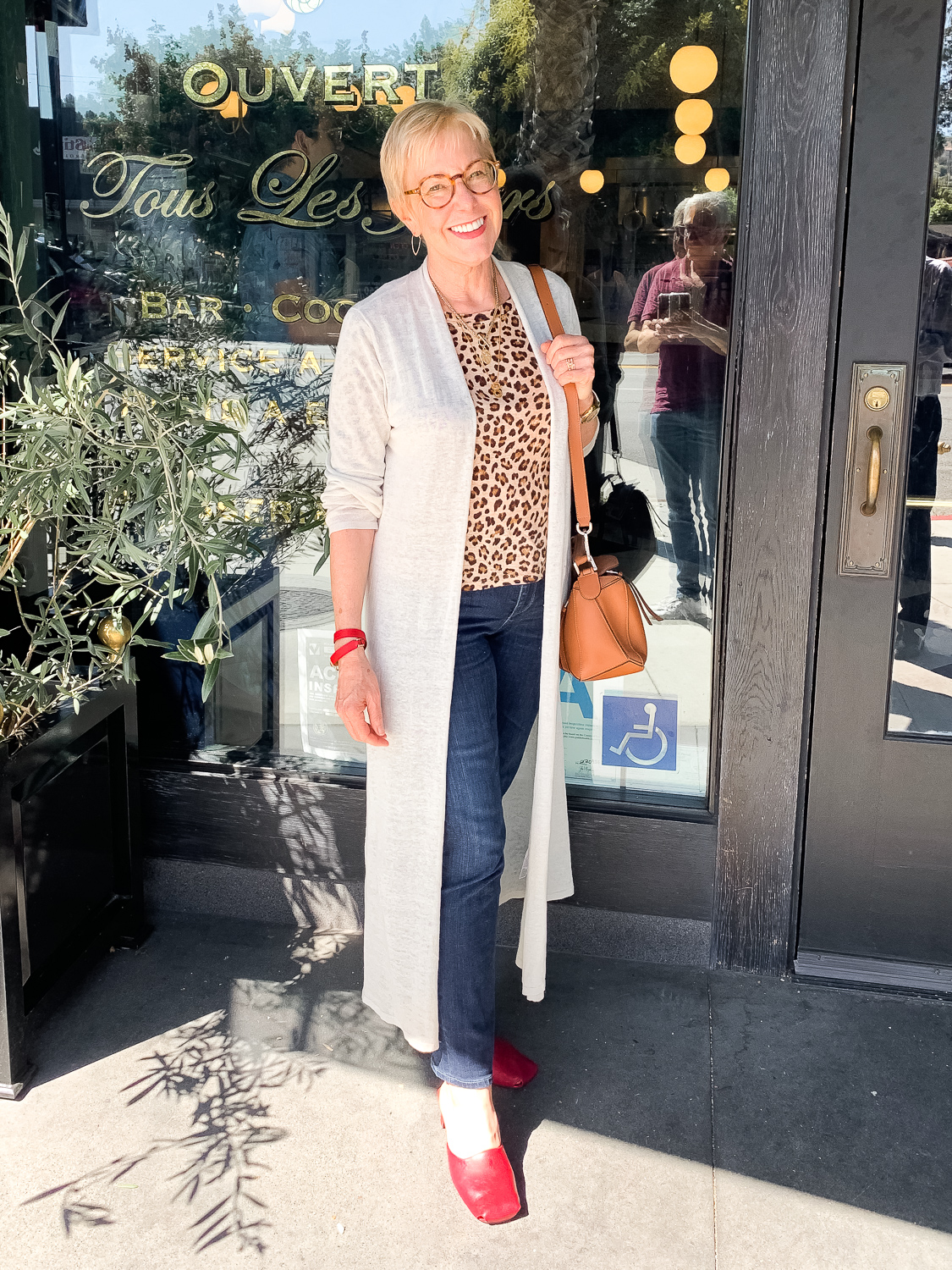 Susan Blakey of une femme d'un certain age wears a casual outfit with a duster cardigan, leopard print tee, jeans and red mules.