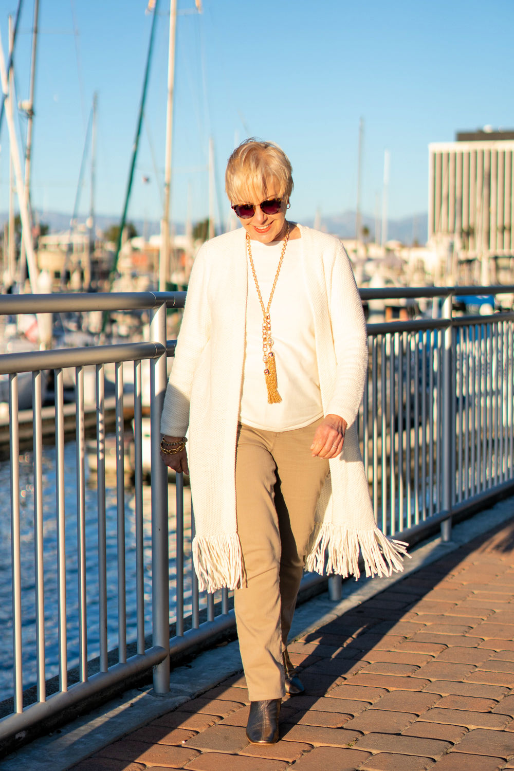 Susan B. of une femme d'un certain age wears a casual holiday party outfit with a fringed cardigan and gold jewelry.