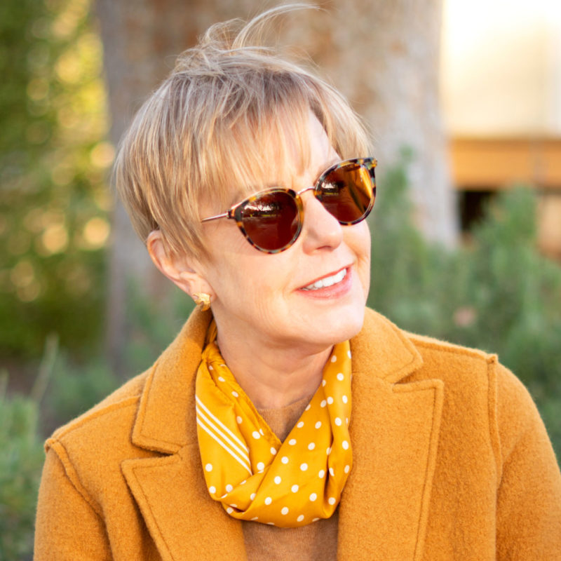 Susan Blakey of une femme d'un certain age wears a mustard polka dot scarf and caramel coat.