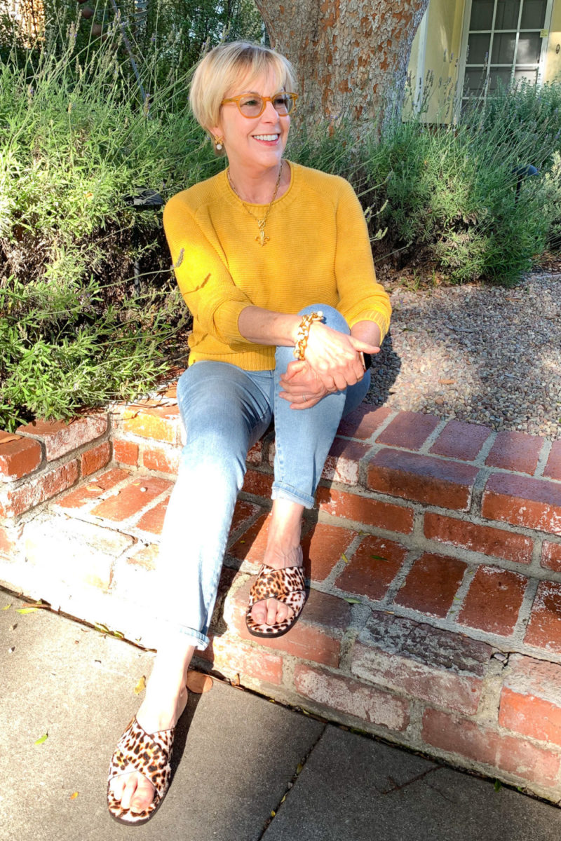 Susan Blakey of une femme d'un certain age wears a gold sweater, French Kande jewelry, and leopard slides.