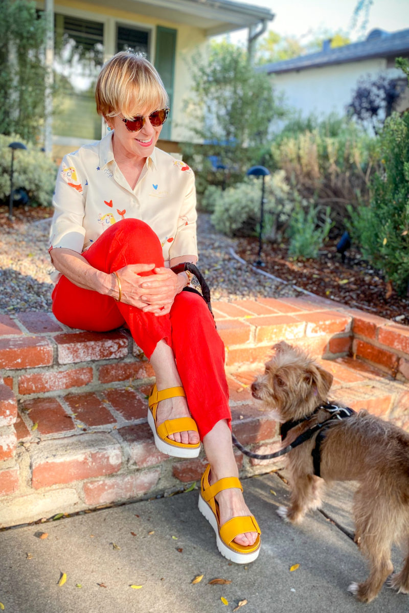 Susan B. of une femme d'un certain age wears a mermaid print shirt, red linen pants and yellow platform sandals.