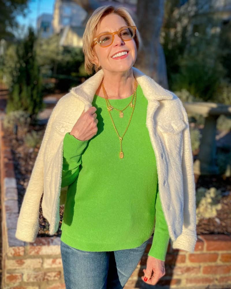 Susan B. wears a green cashmere sweater, layered gold necklaces and a fuzzy trucker jacket. Details at une femme d'un certain age.