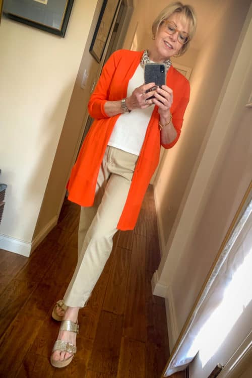 Susan B. wears a long orange cardigan and beige cropped trousers.