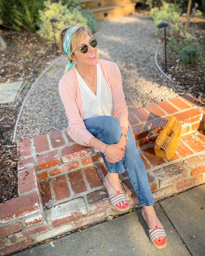 Susan B. of unefemme.net is sitting on front steps wearing a scarf headband, pink cardigan, v-neck top, jeans, and striped espadrille sandals.
