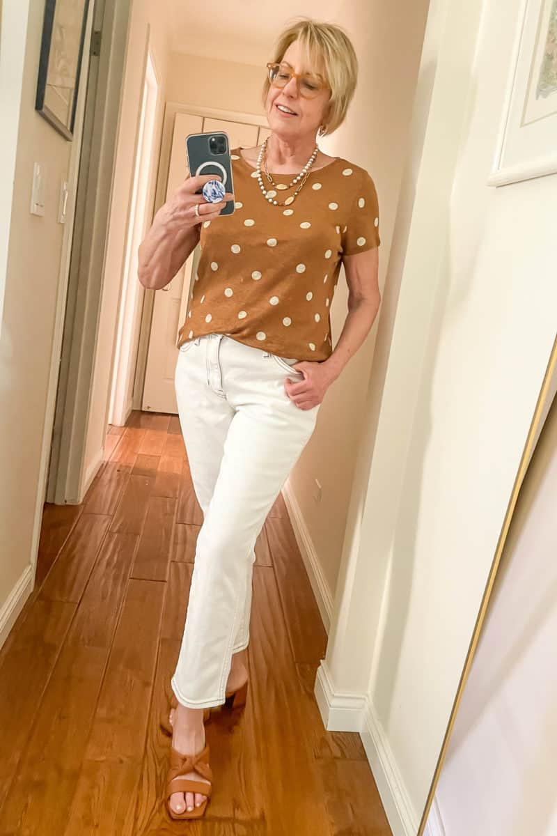 Susan B. wears a white jeans outfit with Sezane polka dot tee, French Kande pearl necklace, and brown Vince sandals.