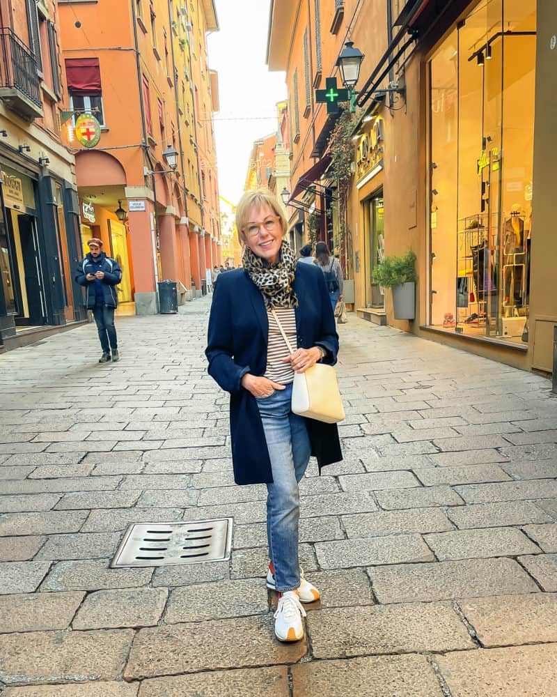 Travel outfits from Italy: Susan B in Bologna wearing a leopard print scarf, navy jacket striped tee, jeans, and white sneakers.