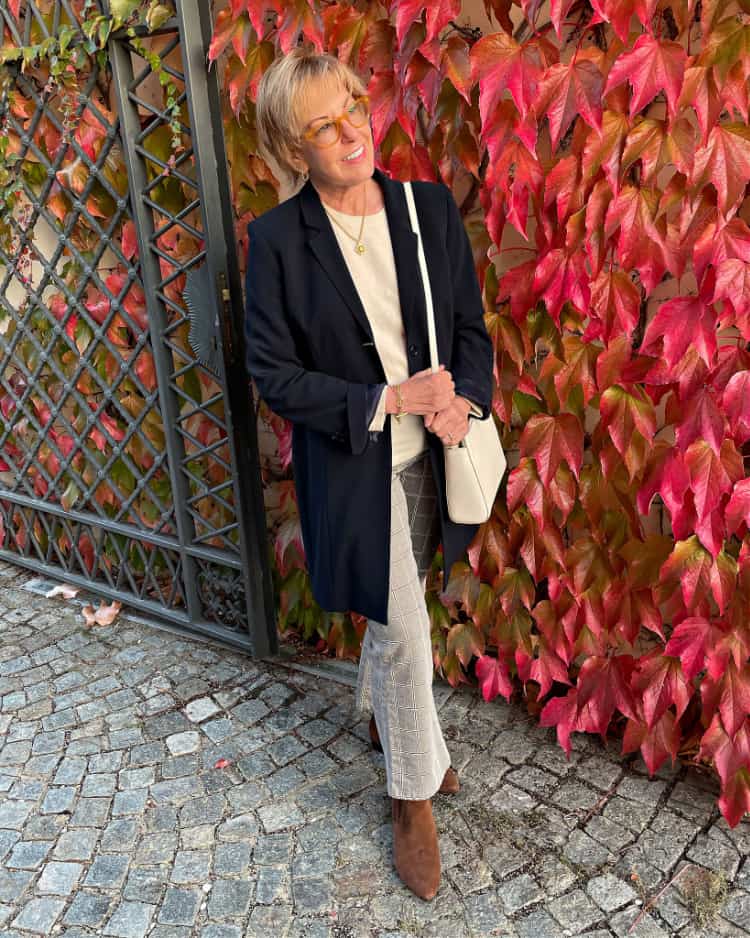 Italy travel outfits: Susan B. wears a long navy blazer, ivory sweater, plaid bootcut jeans and ankle boots.