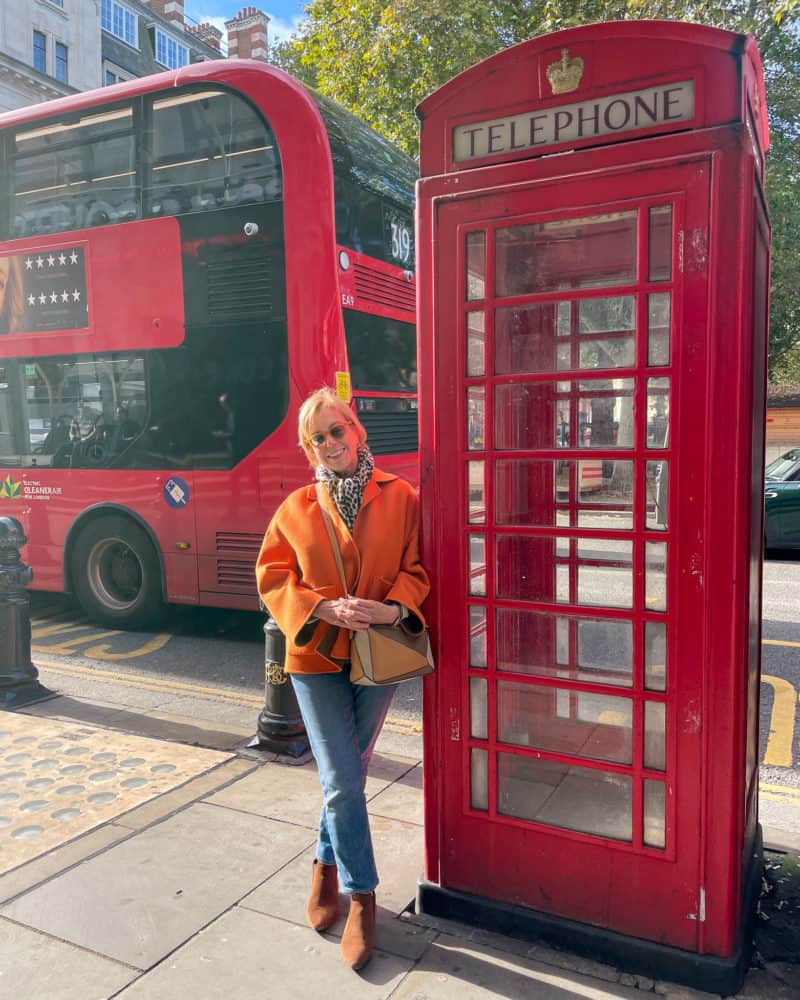 Susan B. in an orange jacket next to a London phone booth with a red bus in the background.