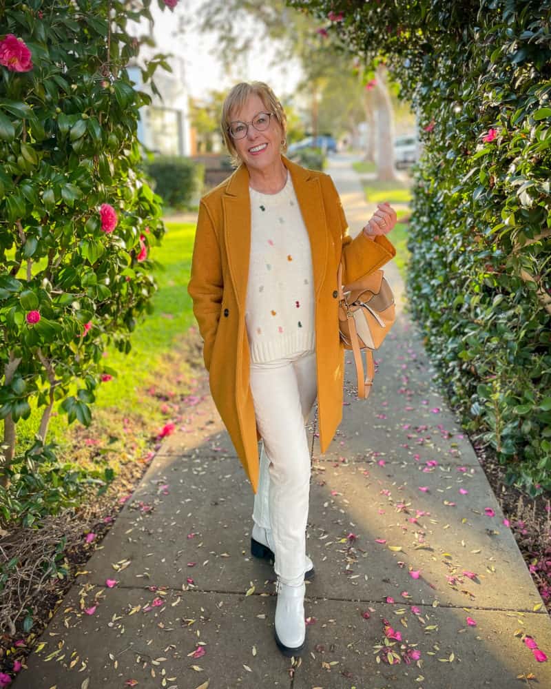 Susan B. wears a gold coat, knot detail sweater, white jeans and ivory lug-sole boots.