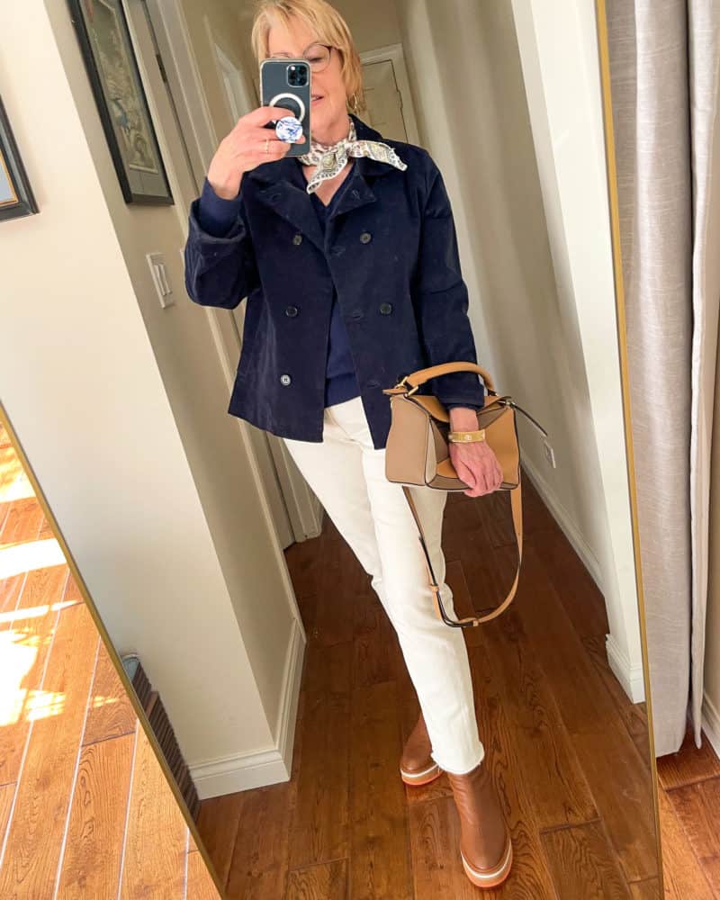 Navy jacket and white jeans outfit: Susan B. wears a peacoat and v-neck sweater, off-white jeans, brown boots, and carries a brown leather bag.