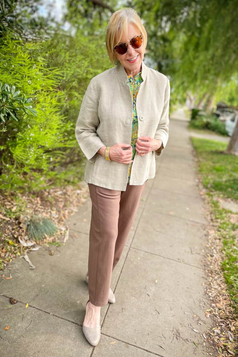 Susan B. wears a beige linen jacket, floral print top, brown knit pants and metallic flats.