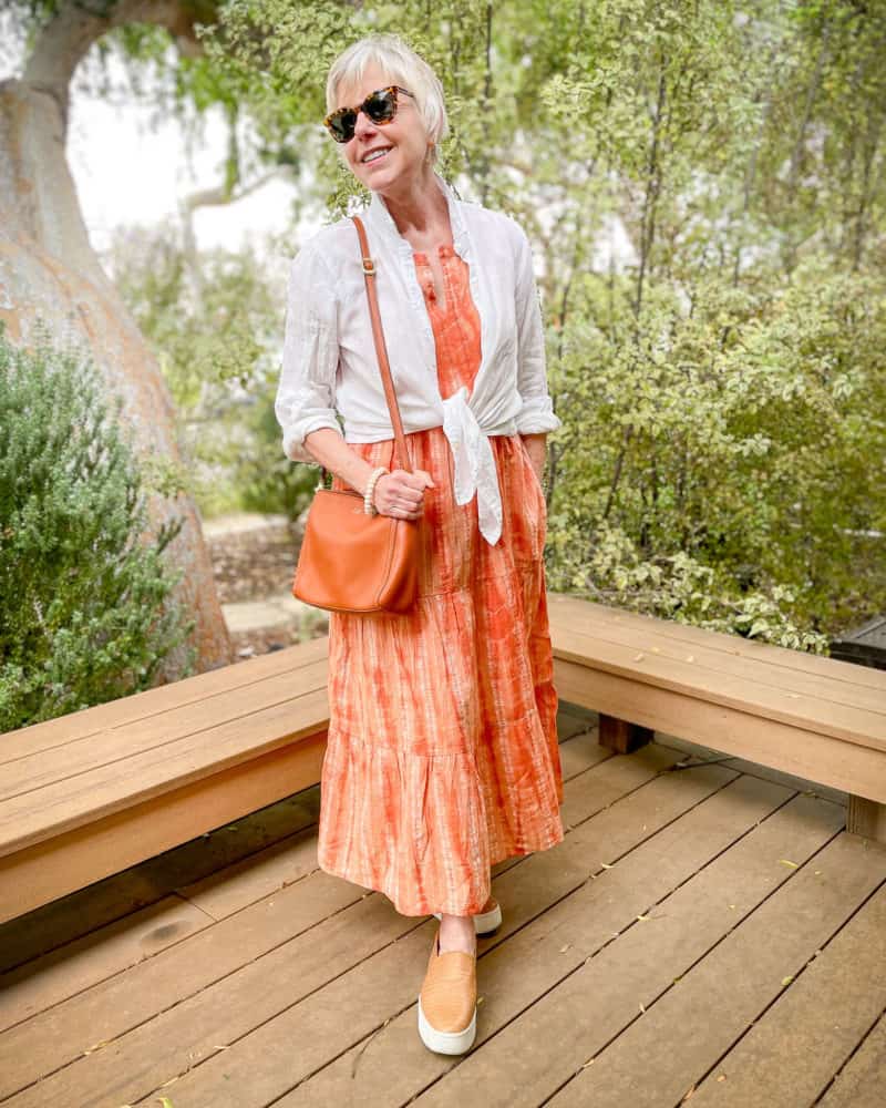 Susan B. wears a white linen shirt tied over a tiered maxi dress, with shoulder bag and platform sneakers.