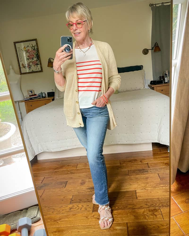 Susan B. wears a beige linen cardigan, red stripe Breton tee, straight leg jeans and flat slide sandals.