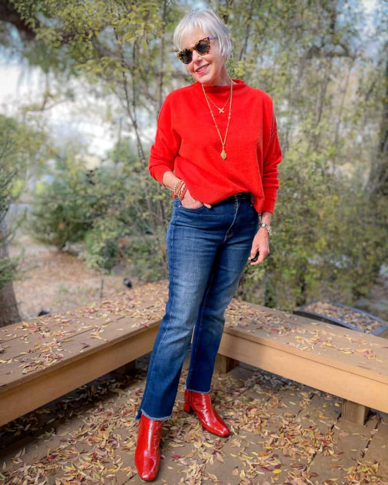 Susan B. wears a casual holiday party outfit with a red sweater, gold necklaces, jeans and sriracha patent boots from gini & albert