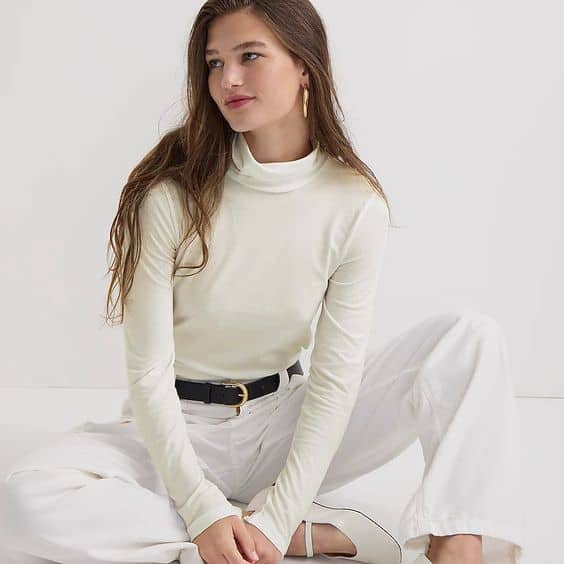 J.Crew tissue turtleneck in Ivory. Woman seated on floor wears ivory turtleneck, white jeans, black belt and white ballet shoes.