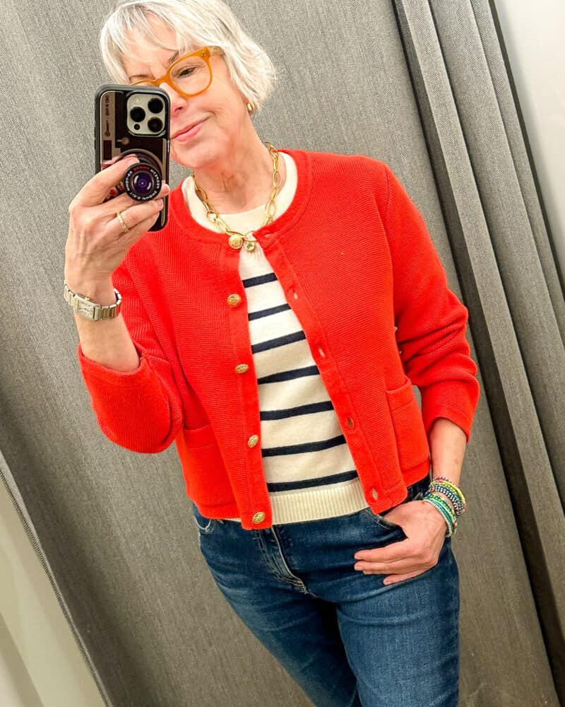 Susan B. takes a mirror selfie wearing a cropped red cardigan with gold buttons, a striped top and blue jeans.