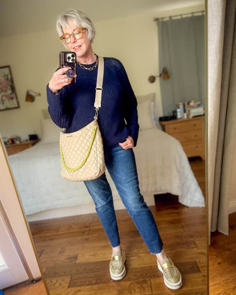 Susan B. wears a navy cotton sweater, slim leg jeans, an MZ Wallace quilted crossbody hobo bag, gold platform loafers.