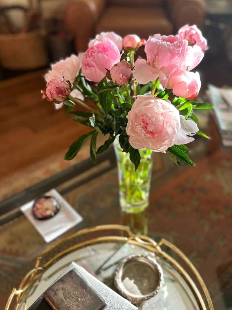 Pink peonies in a glass vase on a table in evening light.
