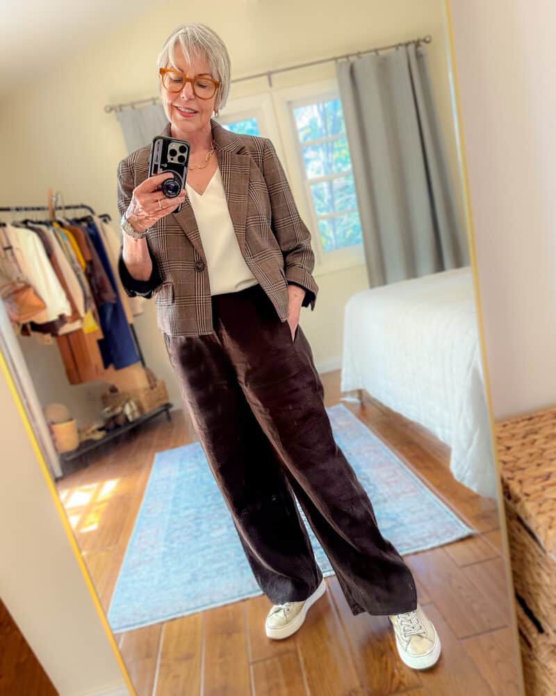 Susan B. wears a cropped plaid blazer, v-neck silk tank, wide leg brown pants, gold sneakers.