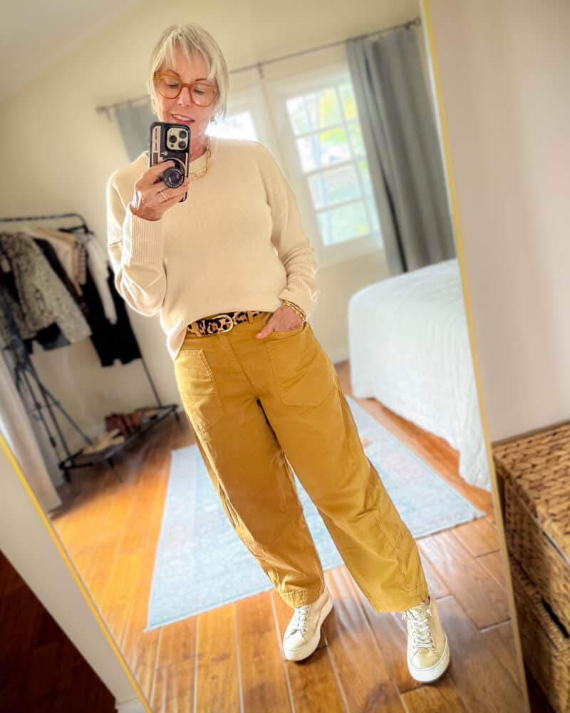 Barrel-leg pants outfit: Susan B wears a cream merino sweater, leopard print belt, Ruti soft twill pants, gold sneakers.