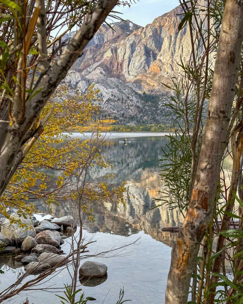 Solitary canoe on Convict Lake with reflections of mountains and fall colors.