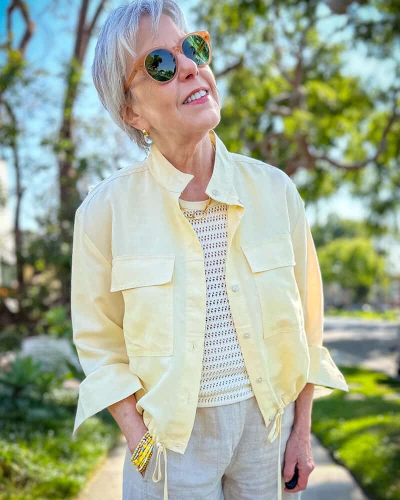 Susan B. wears sunglasses, a crochet tank, linen jacket with drawstring hem, yellow bead bracelets.