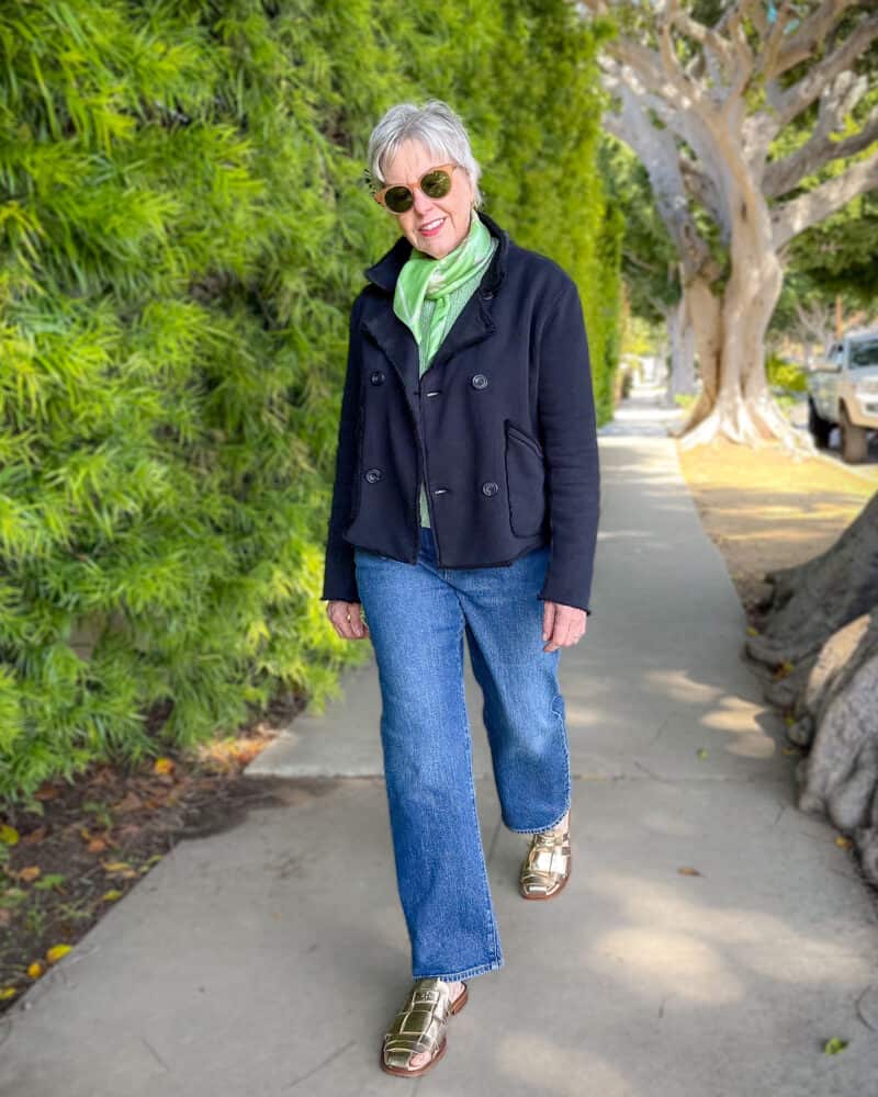 Susan B. wears a navy knit peacoat, green silk scarf and green sweater, blue jeans, and gold fisherman mules