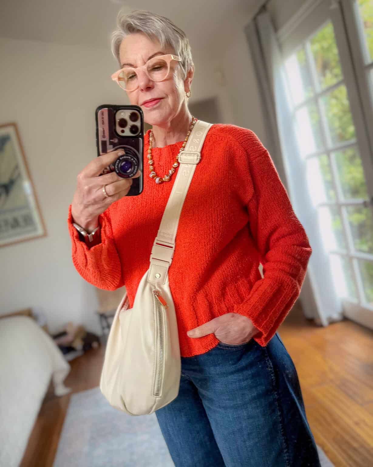 Susan B. shares side view of Lo & Sons Aoyama crossbody bag, also wearing a red sweater, brown bead necklace and blue jeans.