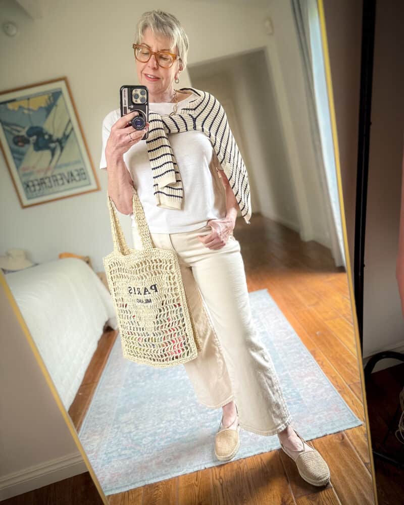 Susan B. wears a striped cardigan tied over shoulders, an ivory tee, ecru jeans, straw "Paris Milano" tote and woven espadrilles.
