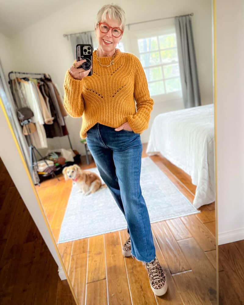 Susan B. wears an alpaca crewneck sweater in "Turmeric," straight-leg jeans, and leopard print sneakers.