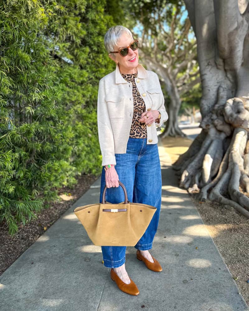 Susan B. wears a beige wool sweater-jacket, leopard print knit shell, barrel leg jeans, brown pointed toe flats and carries a tan suede fan-shape tote bag.