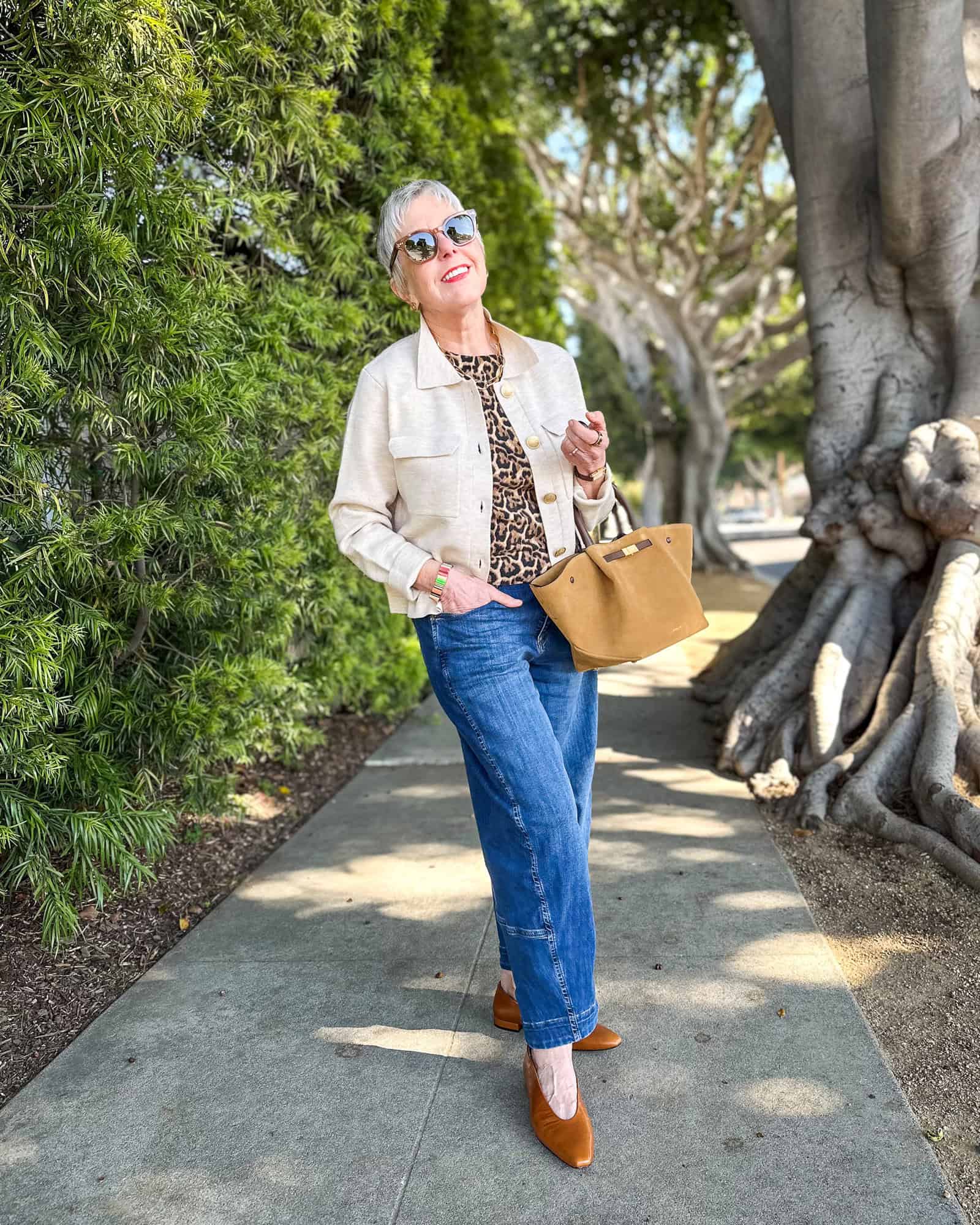 Susan B. wears a beige sweater jacket, leopard print shell, barrel leg jeans, pointed toe flats, and carries a suede tote.