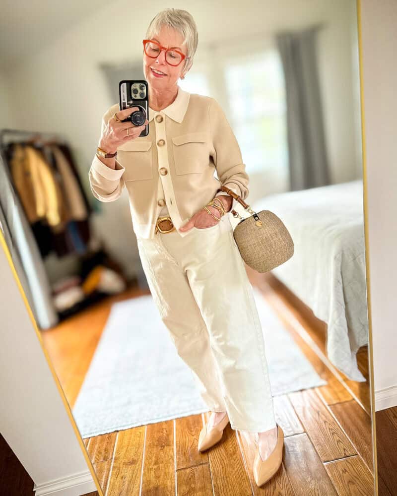 Susan B. wears a beige cardigan with ecru trim, off-white darted-leg jeans, pointed toe flats, basket bag with bamboo handle.