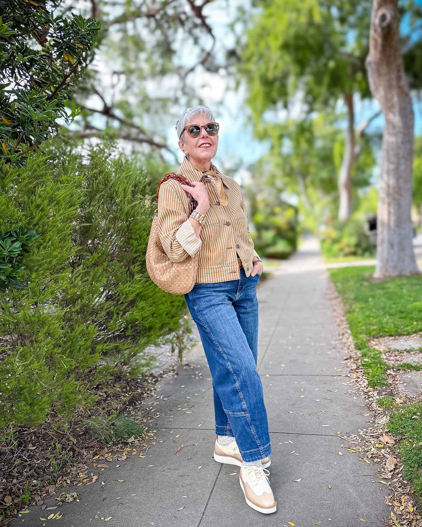 Susan B. wears a striped Me+Em jacket, barrel leg jeans, beige & ivory colorblock oxfords, carries a woven leather bag with resin chain strap.