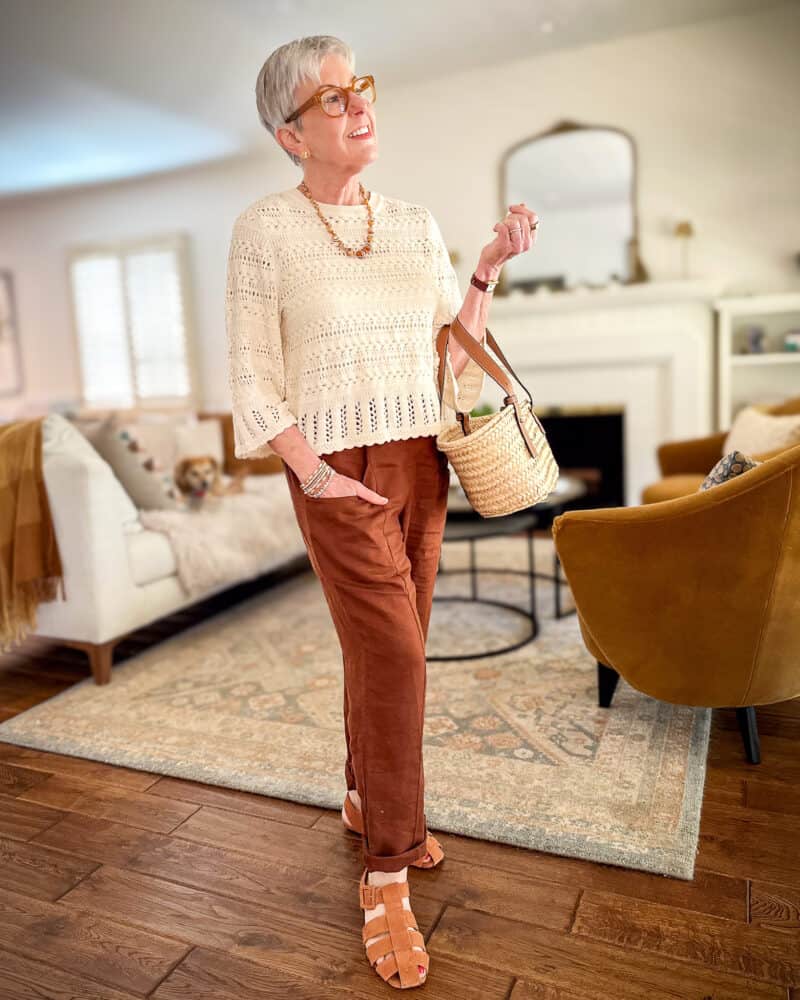 Susan B. wears a Madewell crochet top, brown linen pants, suede fisherman sandals, carries a straw tote.