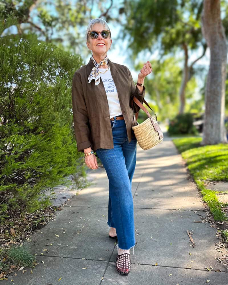 Susan B. wears an Eileen Fisher linen high collar blazer, cotton bandana, graphic tee, straight leg jeans, and jelly sandals.
