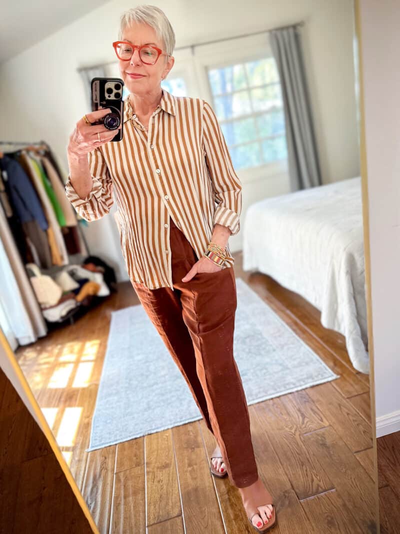 Susan B. wears a striped button-front shirt with brown linen pants and brown low-heel sandals.