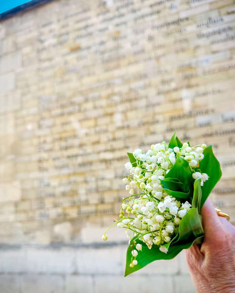 Susan holds a bouquet of muguets (lily of the valley) next to the Rimbaud "bateau ivre" wall in Saint Germain Paris.