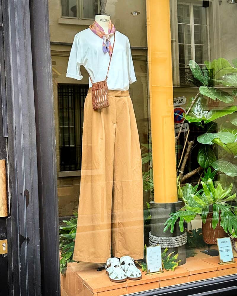 Mannequin in Sessun boutique in Paris wearing a white tee, crossbody bag, amber relaxed trousers.