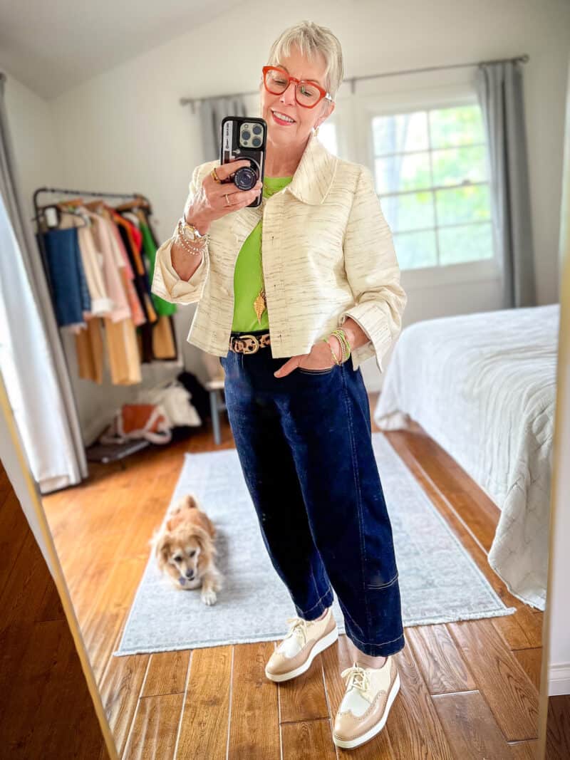 Susan B. wears a blurred stripe swing jacket, green cashmere shell, leopard belt, dark wash jeans, gold jewelry, and two-tone oxfords.
