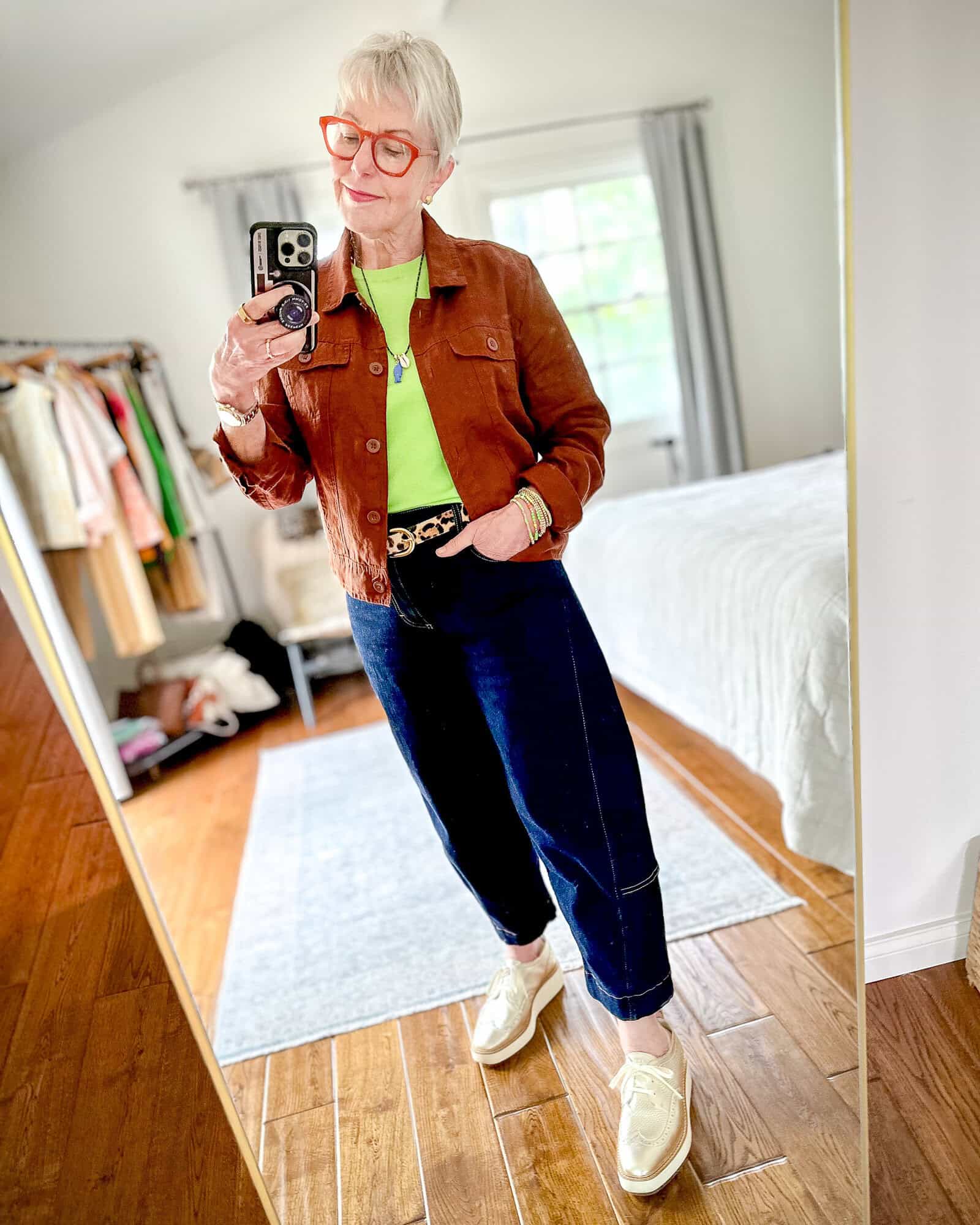 Susan B. wears a brown linen jacket, green cashmere shell, pendant necklace, leopard print belt, dark wash barrel-leg jeans, gold platform oxfords.