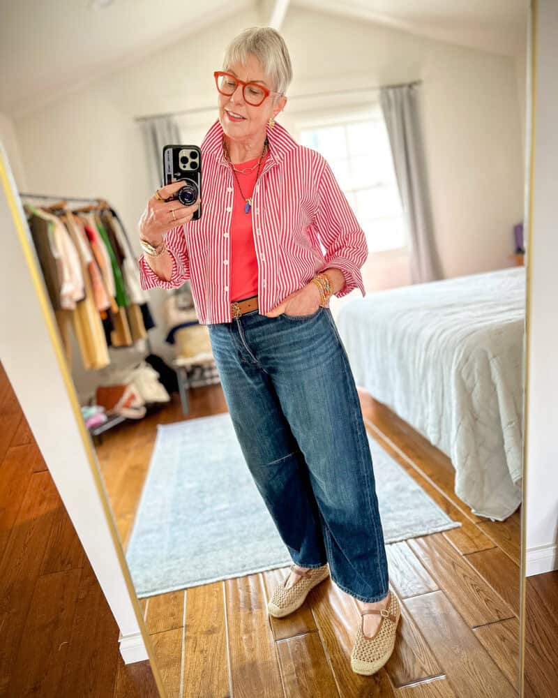 Susan B. wears a red striped cropped cotton poplin shirt, pink lightweight cashmere shell, brown belt, blue jeans, raffia mary jane espadrilles.