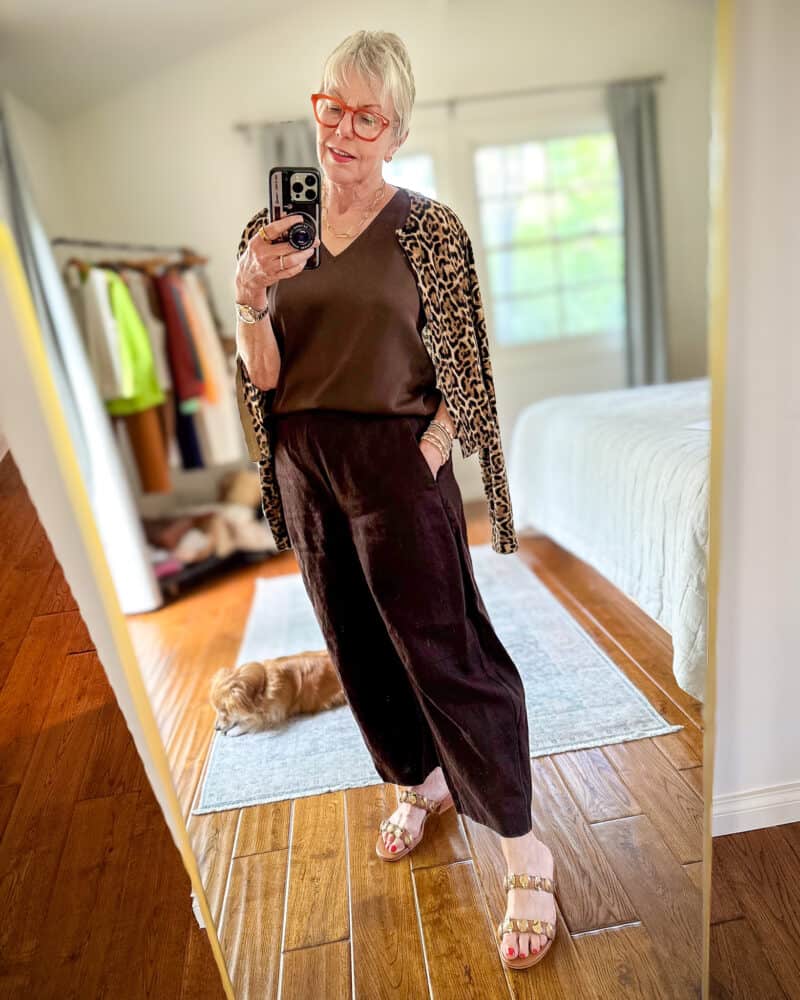 Susan B wear a leopard print cardigan draped over the shoulders with a brown silk tank, brown linen trousers and embellished sandals.