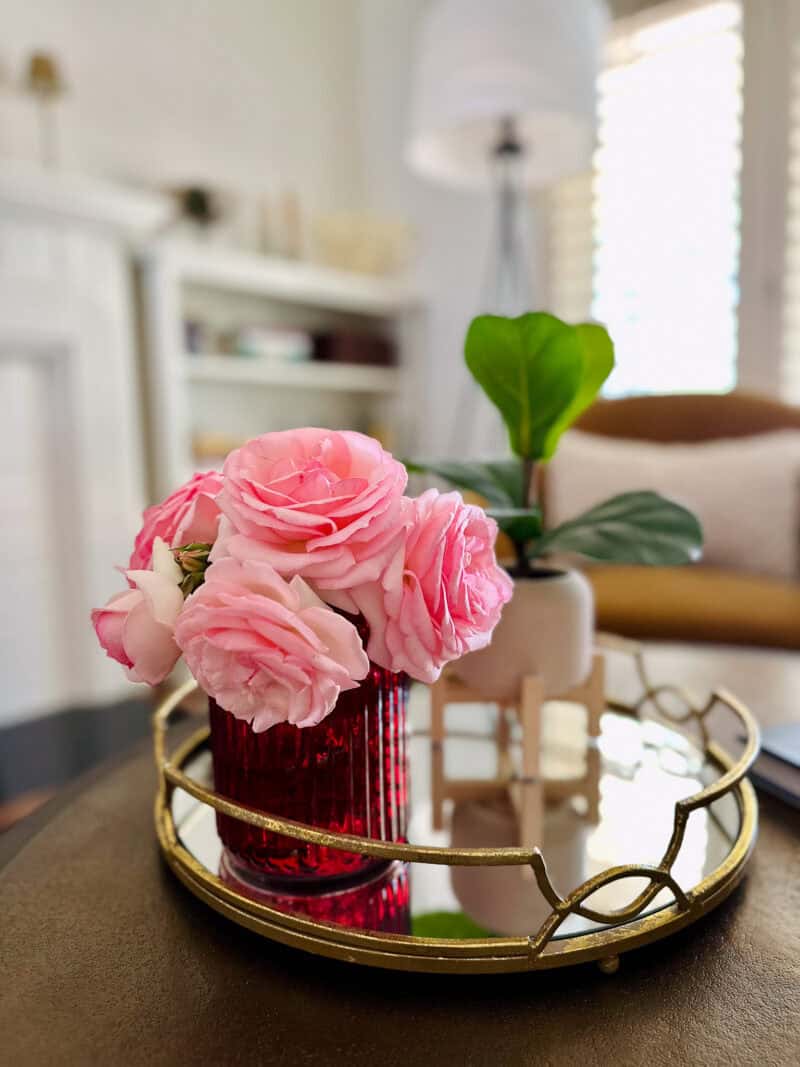 Pink roses in a red mercury glass vase on a mirrored tray on a coffee table.